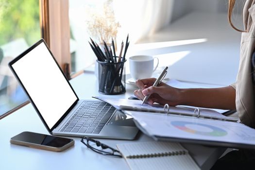 Businesswoman using computer laptop and writing information on document.