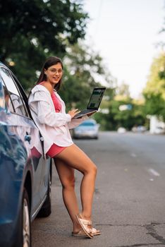A young woman uses a laptop near a car in city center outdoors
