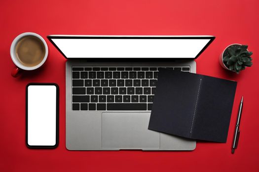 Above view laptop computer, smart phone, coffee cup and notebook on red background.