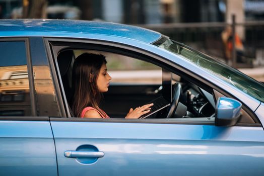 Young woman using laptop in her car while driving. Safe driving concept