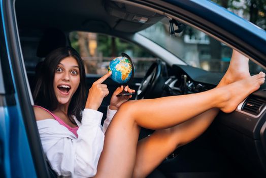 Young woman sitting in a car and holding a globe, travel concept