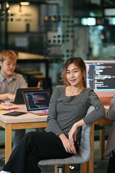 Young female software developer sitting in start up office with co working atmosphere.