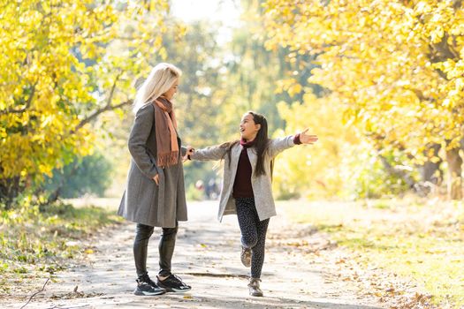 Little girl and her mother enjoy sunny weather in the autumn park.