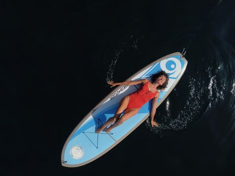 Young attractive brunette woman in red swimsuit, swimming on kayak around volcanic rocks, like in Iceland. Back view. Christmas holiday vacation and travel concept.