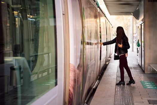 young woman pressing the door button to open the door and board the streetcar, concept of public transportation and urban lifestyle