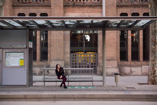 young woman talking on the phone while waiting at the bus stop, concept of public transportation and urban lifestyle