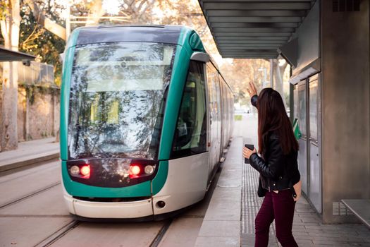 woman raising her hand to call for the streetcar that escapes her, concept of public transportation and urban lifestyle