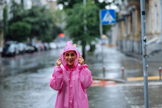 Young smiling woman with a pink raincoat on the street while enjoying a walk through the city on a rainy day.