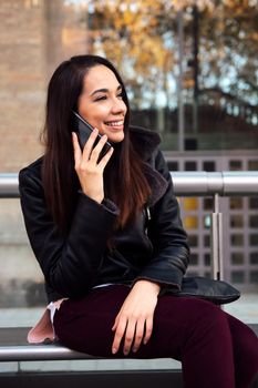 vertical photo of a young woman talking by phone at the bus stop, concept of technology and communication
