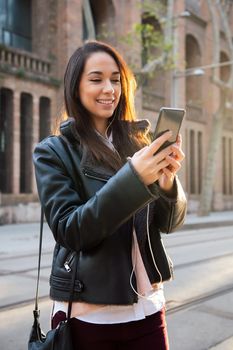 vertical photo of a smiling young woman reading a message at her telephone at the street, concept of technology and communication, copyspace for text