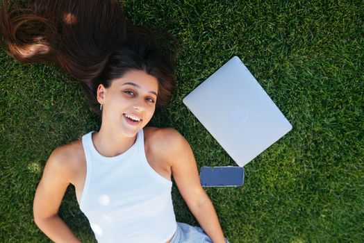 Young fit attractive woman lying on green lawn park. Perks of freelance concept. Background, copy space