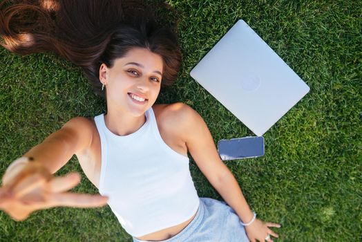 Young fit attractive woman lying on green lawn park. Perks of freelance concept. Background, copy space