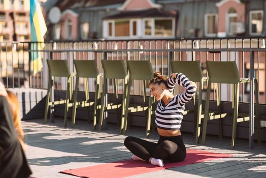 Yogi woman and diverse group of young sporty people practicing yoga, female students training at house's roof. Well being, wellness concept