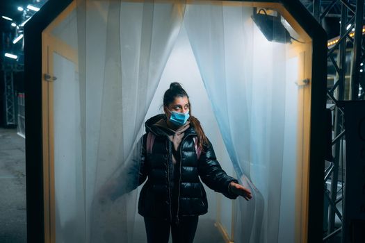 Young beautiful woman in a medic mask is staying in a disinfection tunnel