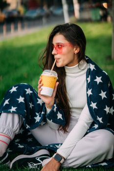 portrait of a young attractive woman in the park with a paper glass of coffee. Rest in the park