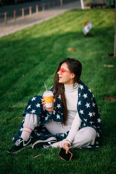 portrait of a young attractive woman in the park with a paper glass of coffee. Rest in the park