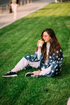 portrait of a young attractive woman in the park with a paper glass of coffee. Rest in the park