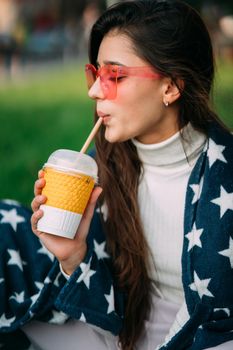 portrait of a young attractive woman in the park with a paper glass of coffee. Rest in the park