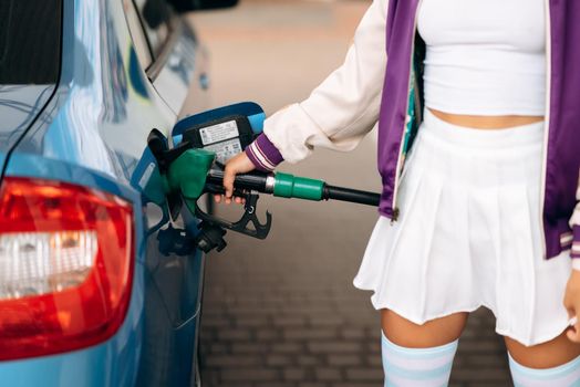 Cheerful young woman brunette filling her car with fuel at a gas station