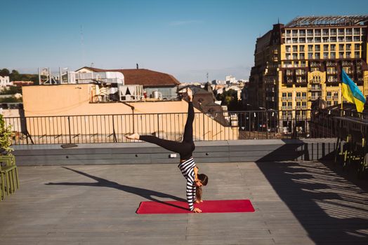 Beautiful young woman working out outdoors and doing yoga handstand exercise on yoga mat