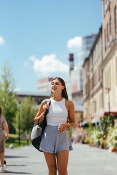 Urban young hipster woman with stylish backpack walks around the city near a building in the spring day. Pretty girl travels.