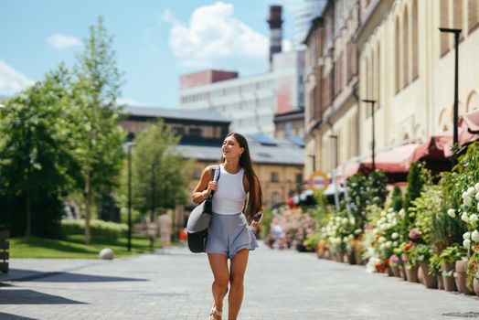 Urban young hipster woman with stylish backpack walks around the city near a building in the spring day. Pretty girl travels.