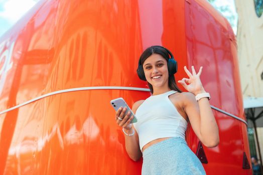Portrait of a happy girl listening music online with wireless headphones from a smartphone in the street