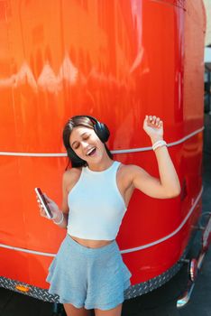 Portrait of a happy girl listening music online with wireless headphones from a smartphone in the street
