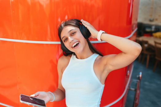 Portrait of a happy girl listening music online with wireless headphones from a smartphone in the street