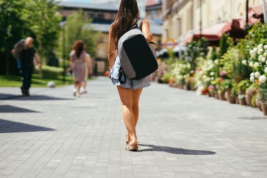 Urban young hipster woman with stylish backpack walks around the city near a building in the spring day. Pretty girl travels.