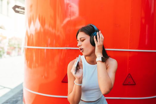 Portrait of a happy girl listening music online with wireless headphones from a smartphone in the street