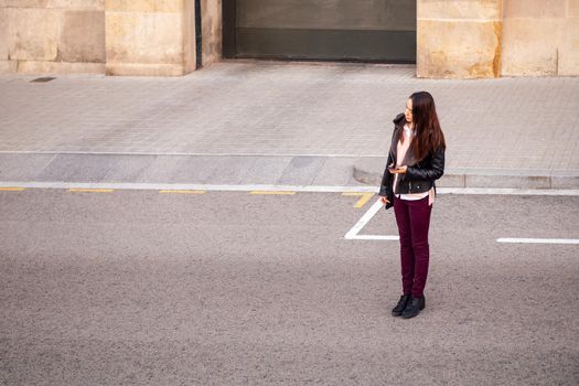 stylish young woman with the phone on the hand waiting a cab by the street side, concept of travel and urban lifestyle, copyspace for text