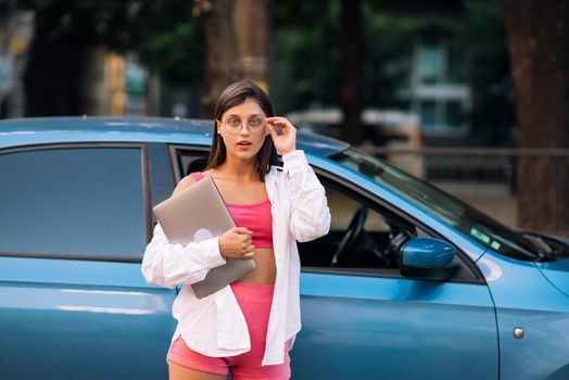 Image of young cheerful beautiful woman walking outdoors holding laptop computer