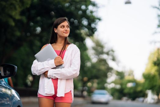 Image of young cheerful beautiful woman walking outdoors holding laptop computer