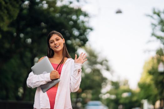 A young woman holding a laptop looks at the camera on the street