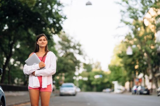 A young woman holding a laptop looks at the camera on the street