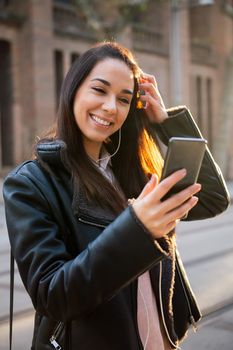 vertical photo of a happy young woman smiling while reading a message at her telephone at the street, concept of technology and communication, copyspace for text
