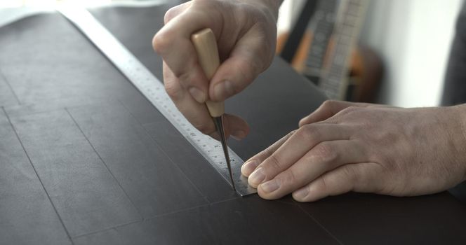 Close up of leather craftsman working with natural leather by awl and ruler. Handmade master at work in local workshop. Leather wallet stitch