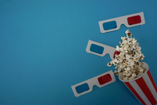 Popcorn is poured on a blue background, on the background are glasses for watching movies. High quality photo