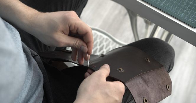 Craftsman sewing a handmade brown leather wallet in workshop