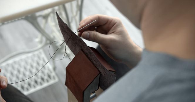 Craftsman sewing a handmade brown leather wallet in workshop