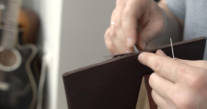 Man working with leather by needle. Genuine Leather. Sewing a purse. Leather work. Tools for sewing bags, wallets, clutches. Stitching. Manual sewing of the product