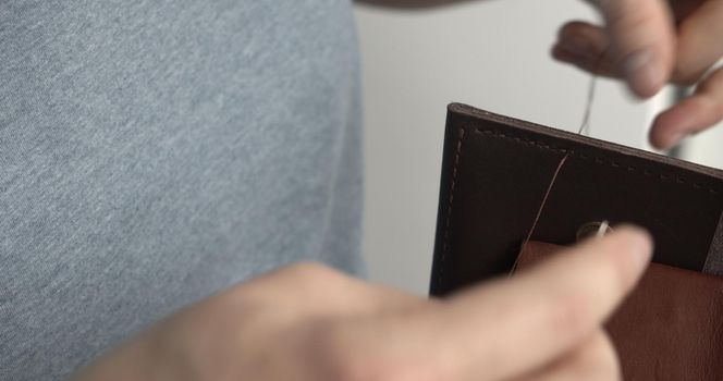 Making a handmade brown leather wallets. The hands of the master sew a leather product