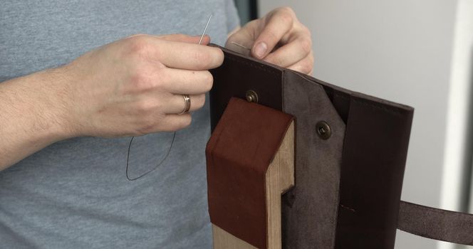 Man working with leather by needle. Tools for sewing bags, wallets, clutches. Stitching