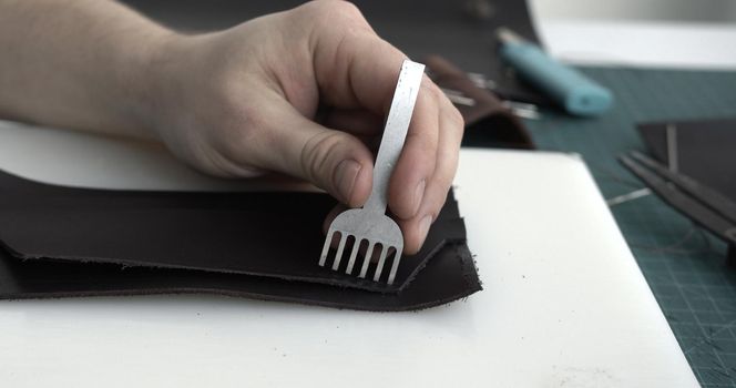 Close up men's hands make a leather product. Punching holes in the leather with a hole punch with a hammer. Tools for leather craft