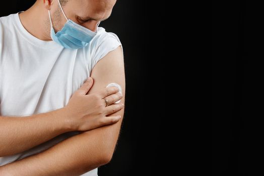 A young man wearing a protective mask holds on to the injection site. A man and a cold and pandemic vaccination. Covid 19. Vaccination for diseases. Copy space.