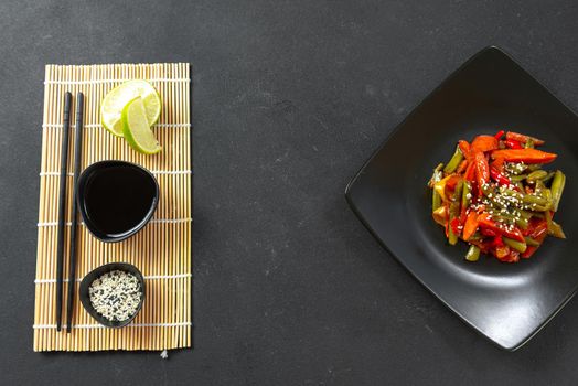 Asian food fried vegetables in teriyaki sauce. Asian vegetables in sweet and sour sauce. Thai vegetables fried in sauce on a black plate on a dark background. Top view and flat lay