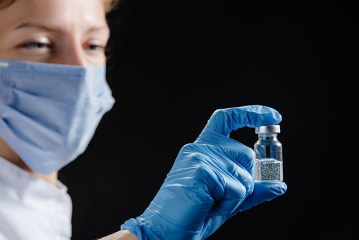 A woman doctor is holding a tube of medicine against a black background. Nurse holding medicine.