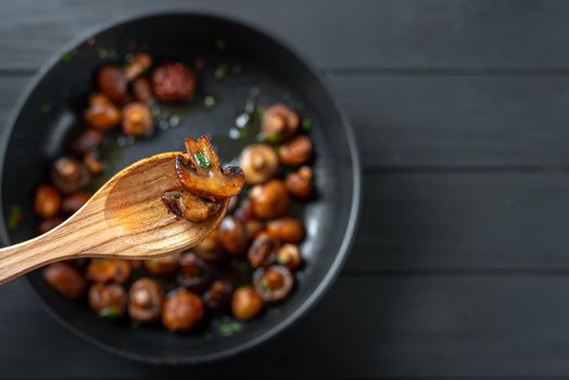 A wooden spoonful of fried mushrooms. Fried mushrooms in the background in defocus. Place for text copy space. Top view. Mushrooms are enriched with a large number of vitamins, including vitamins B1, B2, B6, B12, D12 nicotinic and pantothenic acids, biotonin, etc. Champignons contain a large amount of protein and iron, while being a very low-calorie product