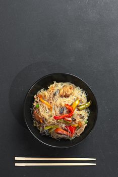 Glass noodle with vegetable in a black bowl on a grey background. Asian food Asian cuisine. Asian or Szechuan noodles. Chinese noodles with vegetables in a black plate. Asian rice or crystal noodles or glass noodles with vegetables. This is a classic Asian dish. Top view and flat lay with copy space for text. Empty space